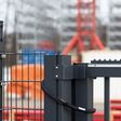 Neuer Sicherheitszaun aus Metall und Stacheldraht, moderne Toranlage mit Vorhängeschloss vor einer Großbaustelle