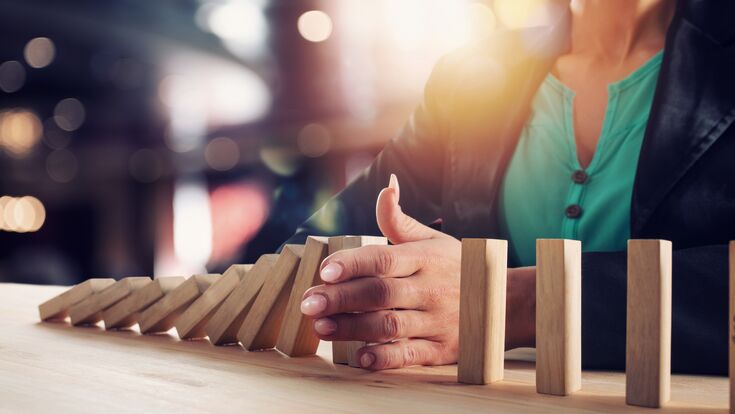 © alphaspirit - stock.adobe.com Businesswoman stops a chain fall like domino game toy. Concept of preventing crisis and failure in business