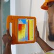 Close up of african professional worker doing analysis of heat on wall with thermal imaging camera. Afro-american builder using infrared imaging app on tablet doing house renovation