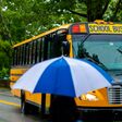 Dame mit Regenschirm vor Schulbus