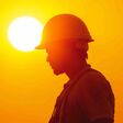 A silhouette of a construction worker wearing a hard hat, standing against a bright orange sunset. The sun is behind the worker, creating a halo effect. The image represents hard work, dedication, and resilience in the face of extreme heat.