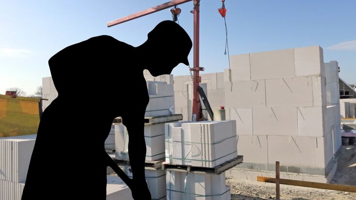 Schwarze Silhoutte eines Bauarbeiters mit Schaufel, im Hintergrund ein Rohbau