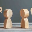 Two wooden figures engaged in a conversation with speech bubbles on a dark gray background, symbolizing dialogue and interaction with a minimalist aesthetic.