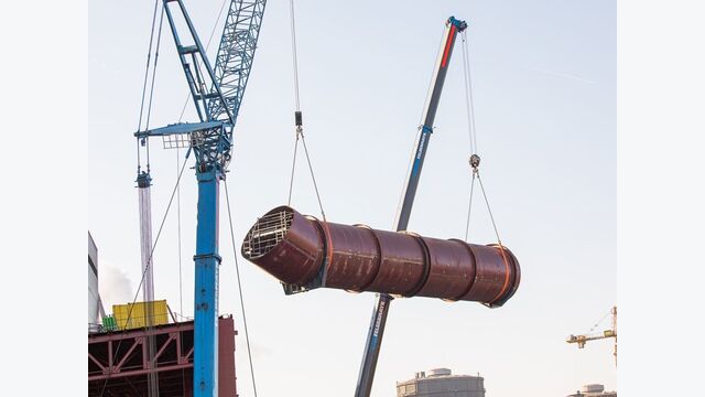 Zwei Krane heben ein Segment der Entstaubungsleitung ein. Die Rohrleitung besitzt einen Durchmesser von 5,6 Metern; angeliefert wurden bis zu zwölf Meter lange Einzelschalen.