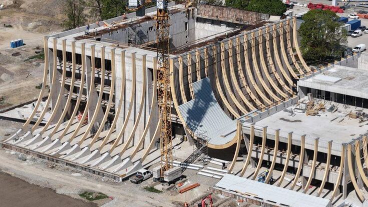 Im Bauzustand wird die Konstruktion hinter der späteren Fassade sichtbar: Gebogene Brettschichtholzträger spannen zwischen den massiven Hallenvolumen und formen den zentralen Zwischenraum der EVE Music Hall.
