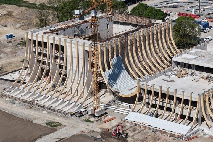 Im Bauzustand wird die Konstruktion hinter der späteren Fassade sichtbar: Gebogene Brettschichtholzträger spannen zwischen den massiven Hallenvolumen und formen den zentralen Zwischenraum der EVE Music Hall.