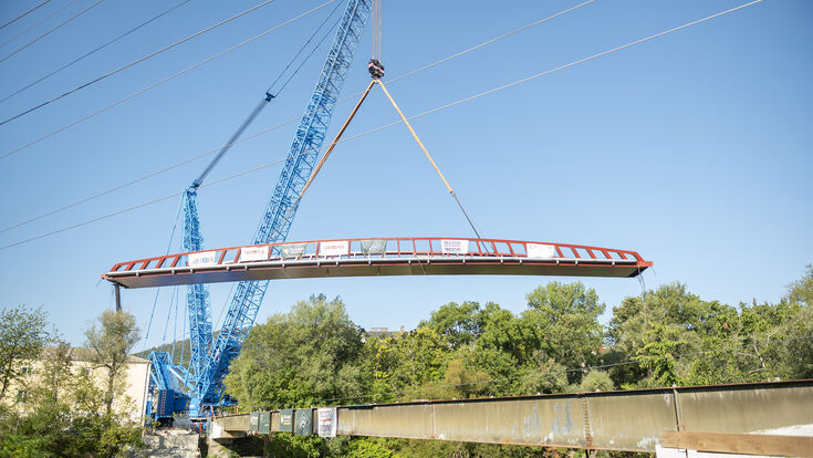 Rund 280 Tonnen Stahl in der Luft: Das vollständig montierte Tragwerk des neuen Pongratz-Moore-Stegs wurde am 24. August mit einem Liebherr LR 11000 über die Mur gehoben und an seine endgültige Position manövriert.