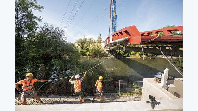 Zentimeterarbeit am Widerlager: Mitarbeiter hielten das schwebende Tragwerk während des letzten Teils des Manövers mit Führungsseilen auf Kurs, bevor es auf den vorbereiteten Lagern abgesetzt wurde.