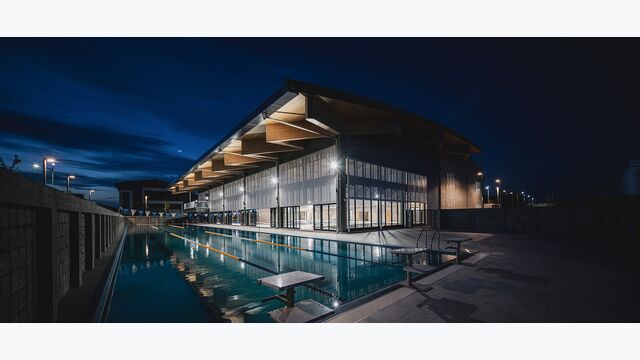 Das Dounan Sports Centre verfügt neben dem Hallenbad auch über ein 50 Meter langes Außenbecken. Die Aufnahme zeigt die fertiggestellte Anlage in der Abenddämmerung.