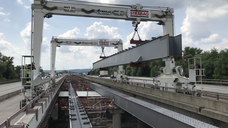 Zwei Portalkrane heben einen gewaltigen Stahlhohlkastenträger zwischen die bestehenden Fahrbahnen der Hochstraße Elbmarsch. Insgesamt wurden für die Erweiterung Deutschlands längster Autobahnbrücke 195 Stahlhohlkastenträger montiert.