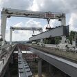 Zwei Portalkrane heben einen gewaltigen Stahlhohlkastenträger zwischen die bestehenden Fahrbahnen der Hochstraße Elbmarsch. Insgesamt wurden für die Erweiterung Deutschlands längster Autobahnbrücke 195 Stahlhohlkastenträger montiert.