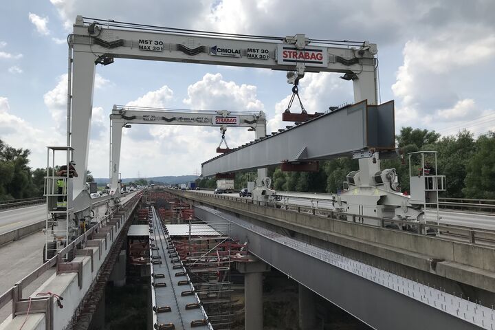 Zwei Portalkrane heben einen gewaltigen Stahlhohlkastenträger zwischen die bestehenden Fahrbahnen der Hochstraße Elbmarsch. Insgesamt wurden für die Erweiterung Deutschlands längster Autobahnbrücke 195 Stahlhohlkastenträger montiert.