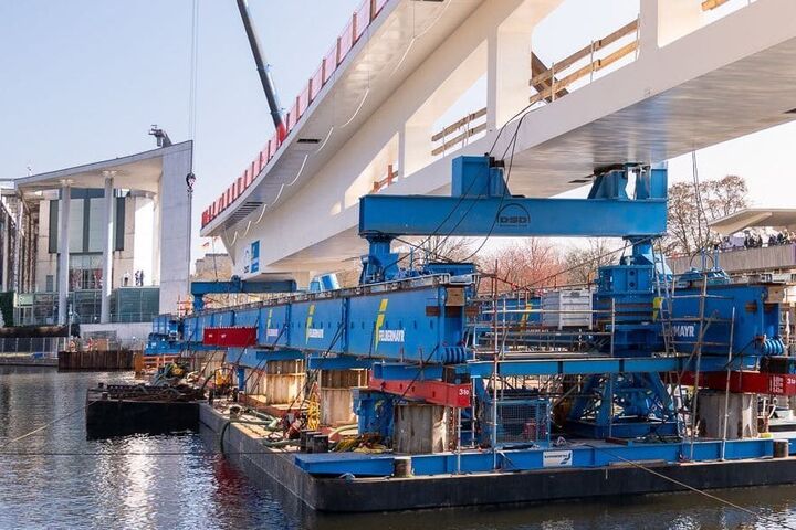 Eine rund 1.500 Tonnen schwere Stahlbrücke wird am Berliner Bundeskanzleramt über die Spree verschoben. Für die aufwendige Montage setzte die österreichische Felbermayr-Gruppe unter anderem schwimmende Pontons und spezielle Schwerlasttechnik ein.